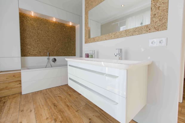 Modernes Badezimmer im Musterhaus mit Doppelwaschbecken, Holzoptikboden, großer Spiegelwand und Badewanne.