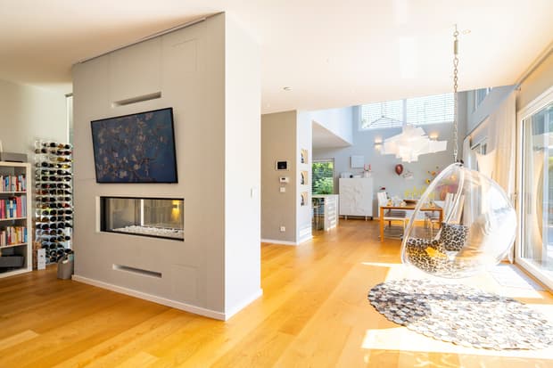 Moderner Wohnraum mit hellen Holzböden, hängendem Acryl-Ei-Sessel und integriertem Kamin in offener Raumgestaltung