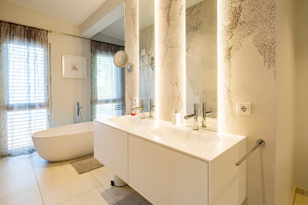 Modernes Badezimmer mit freistehender Badewanne, Doppellavabo, beleuchteten Spiegeln und transparenten Gardinen