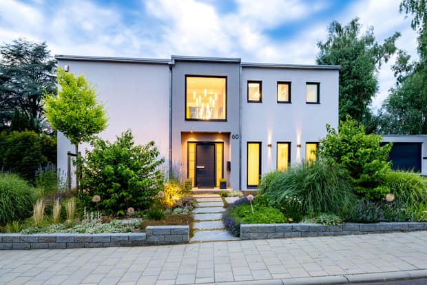 Modernes zweistöckiges Haus mit weißer Fassade, großer Fensterfront und gepflegtem Garten mit Zierpflanzen und Beleuchtung