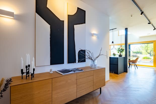 Moderner Flur mit Holzsideboard, schwarzem Kerzenhalter, abstrakter Wandkunst und Blick in helle Wohnküche mit Gartenblick