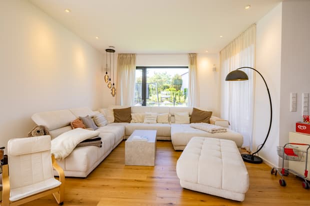 Helles Wohnzimmer mit großer weißer Cord-Eckcouch, Holzboden, Stehlampe und bodentiefem Fenster mit Blick in den Garten