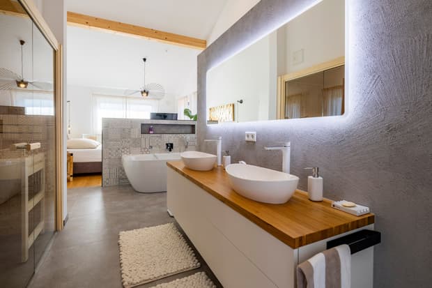 Modernes Badezimmer mit Holzarbeitsplatte, weißen Aufsatzwaschbecken, Badewanne und großer Spiegelwand mit LED-Beleuchtung