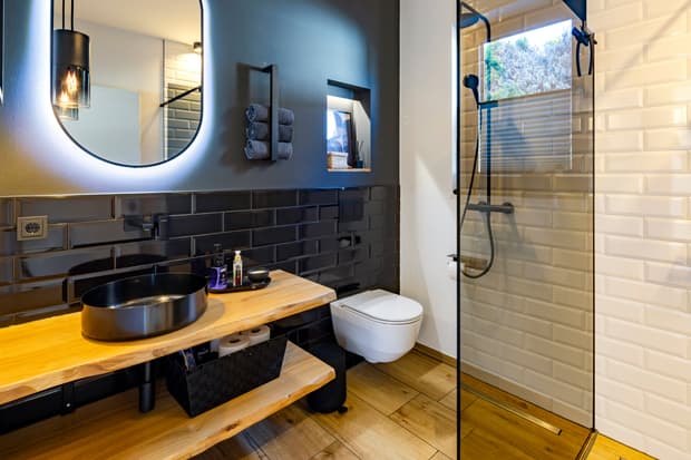 Modernes Badezimmer mit schwarzem Waschbecken, Holztisch, Glas-Duschabtrennung und weißen sowie schwarzen Wandfliesen