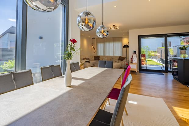 Moderner Essbereich mit großem rechteckigem Tisch, grauen und pinken Stühlen, Kugelpendelleuchten und Blick in den Garten