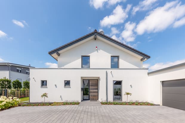 Modernes weißes Einfamilienhaus mit Pultdach, Holz-Haustür und großer Garagentür an sonnigem Tag