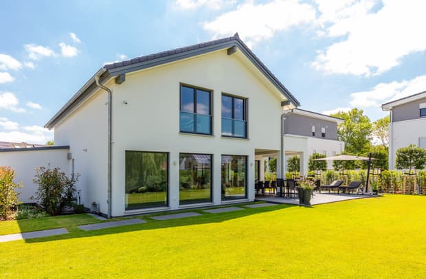 Modernes zweistöckiges Haus mit weißer Fassade, großen Fenstern und gepflegtem Garten in sonniger Vorstadtlandschaft