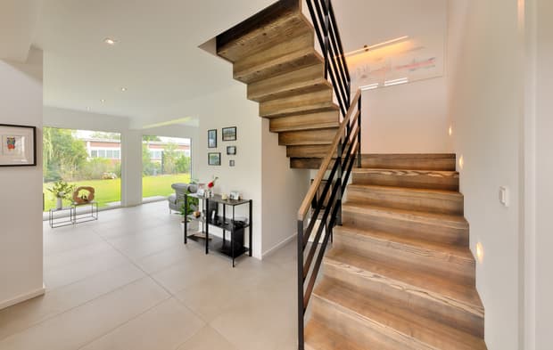 Offener Eingangsbereich mit Treppe aus Holz und Metallgeländer sowie großen Fenstern und Blick auf grünen Garten