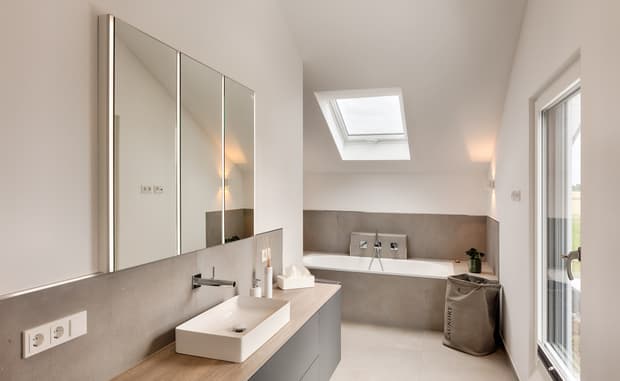 Moderner heller Badezimmer mit rechteckigem Waschbecken, Holzarbeitsplatte, grauem Waschbeckenunterschrank und Badewanne unter Dachfenster