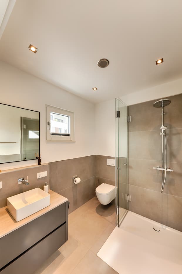 Modernes Bad mit eckiger weißer Waschschale, grauem Unterschrank, bodengleicher Dusche mit Glasabtrennung und wandhängendem WC