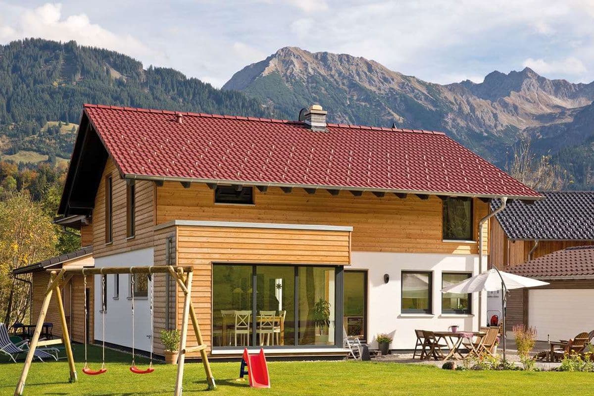 Alpenhaus mit Satteldach, kubischem Anbau und Schneefangsystem mit Bergen im Hintergrund