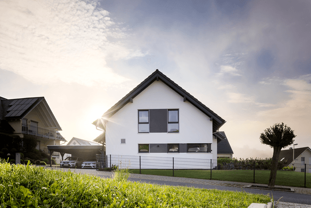 Modernes Einfamilienhaus mit weißer Fassade und dunklem Satteldach im Sonnenaufgang mit Garten und Nachbarhäusern