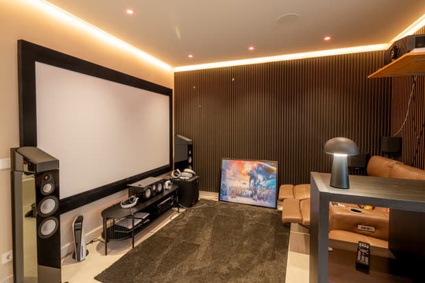 Modernes Heimkino mit großer Leinwand, braunem Ledersofa, schwarzem Teppich, Holzpaneelen und moderner Beleuchtung