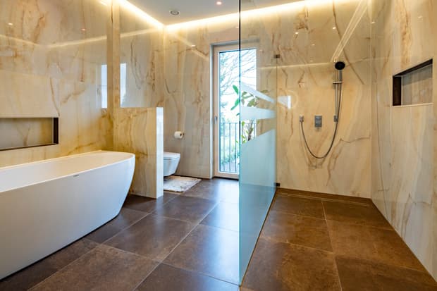 Modernes Badezimmer mit freistehender Badewanne, offener Glasdusche, weißem WC und Boden aus braunen Fliesen