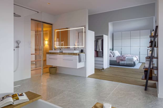 Modernes Musterhaus mit offenem Bad, Doppelwaschbecken, begehbarem Kleiderschrank und hellem Schlafzimmer mit Holzboden.