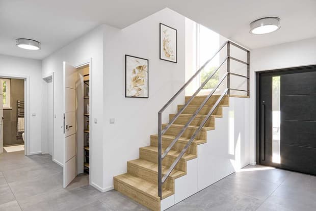 Moderner heller Flur mit Holztreppe, schwarzer Eingangstür, grauem Fliesenboden und weißen Wänden mit Deko-Bildern