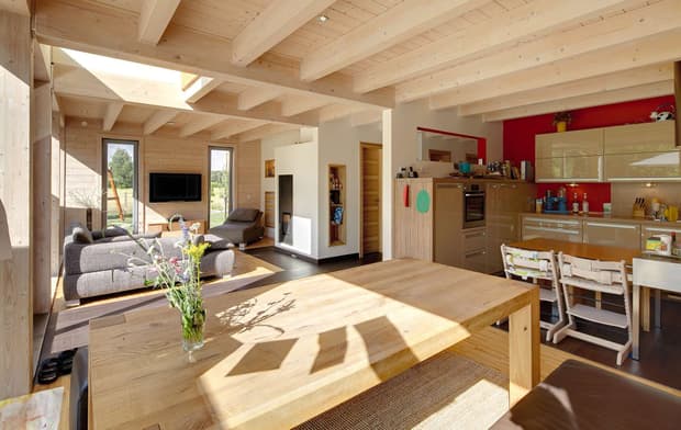 Der Wohn- und Essbereich des Holzhauses im Landhausstil mit durchgängiger Holzfassade und großer Glasfront