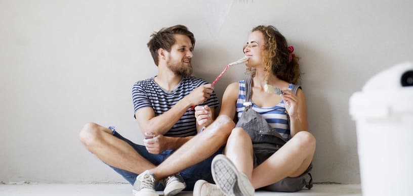 Mann und Frau sitzen auf dem Boden vor einer frisch gestrichenen Wand