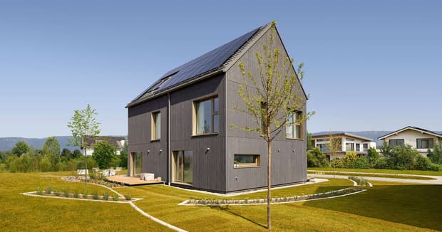 Modernes nachhaltiges Musterhaus mit Holzfassade, Satteldach, Solarpanelen und gepflegtem Garten in ruhiger Wohnlage.