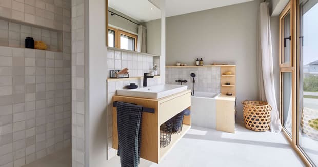 Modernes Badezimmer im Musterhaus mit Holzwaschtisch, Badewanne, großer Fensterfront und heller, minimalistischer Einrichtung.