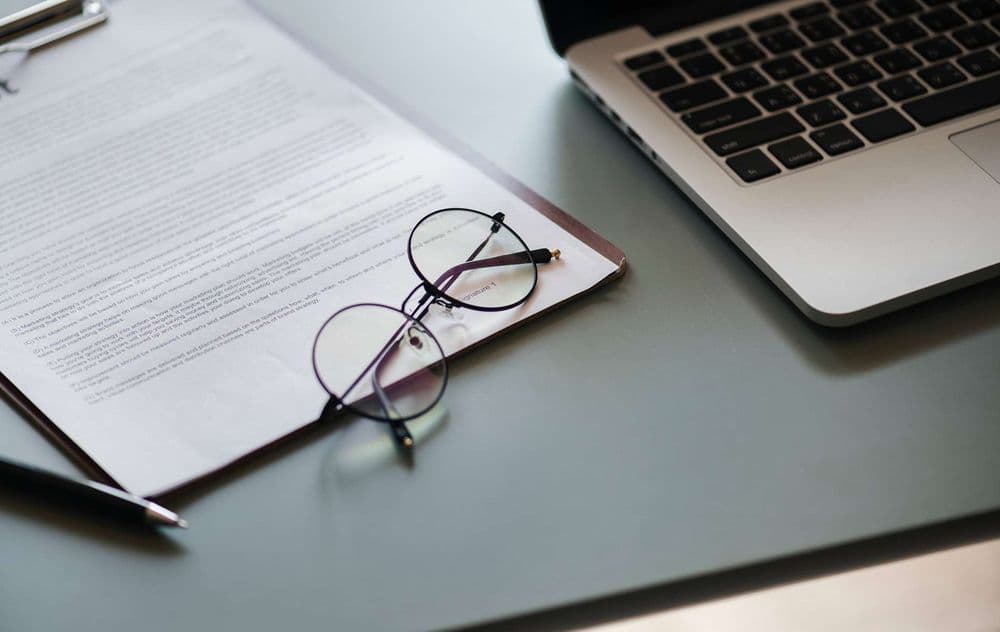 Schreibtisch mit Notebook, Brille, Stift und Unterlagen