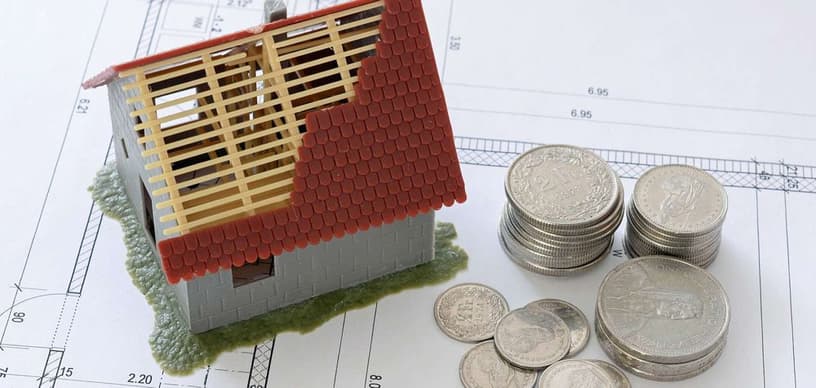 Kleines Haus und mehrere Münzen auf einer Grundrisszeichnung