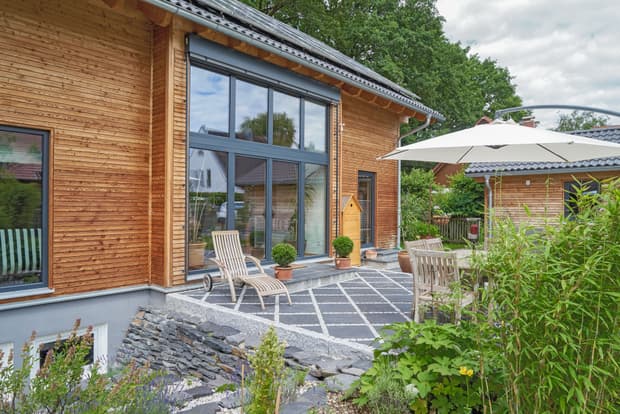 Die Terrasse des Holzhauses im Landhausstil, Lärchenfassade, große Glasfront, moderne Technik