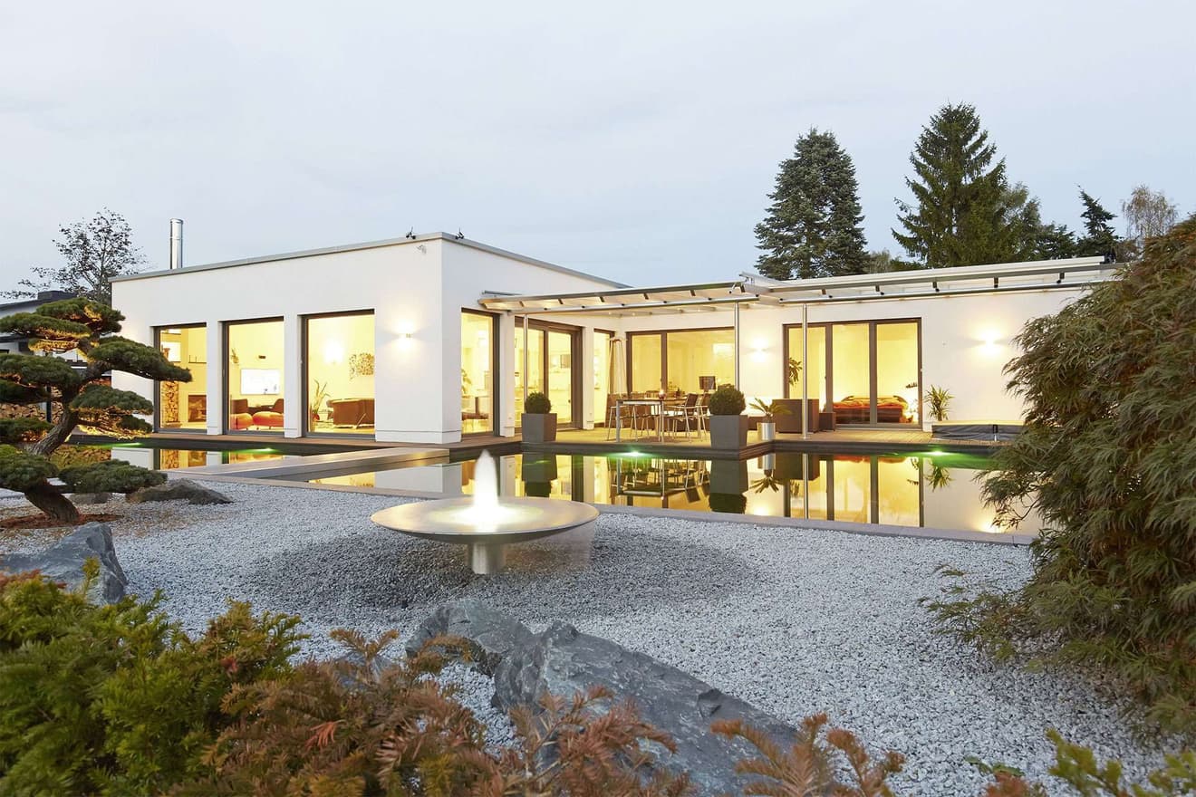 Modernes Fertighaus im Kubusstil mit überdachter Terrasse und Gartenteich