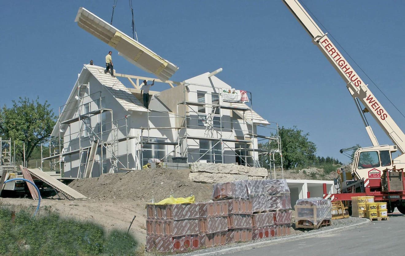 Bauarbeiter beim Aufbau des Dachstuhls mithilfe eines Krans