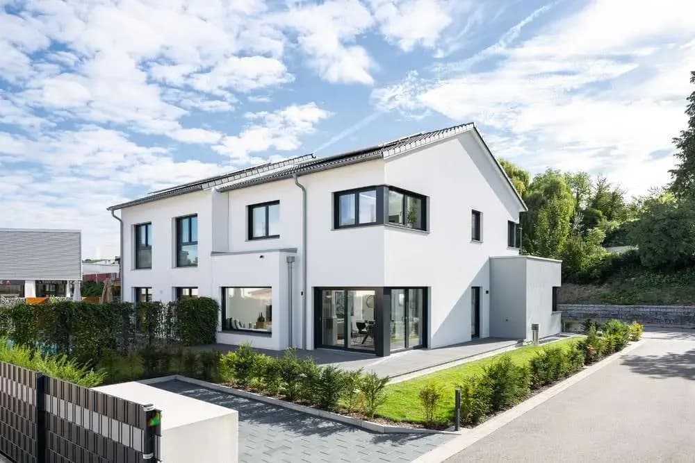 Modernes Doppelhaus mit weißer Fassade, Flachdach, großen Fenstern, Einfahrt, Vorgarten und gepflegter Begrünung.