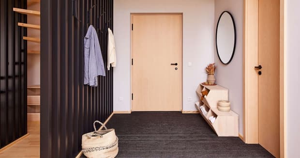 Moderner Eingangsbereich im Musterhaus mit Holzdetails, schwarzer Wandverkleidung, Garderobe und stilvoller Dekoration.