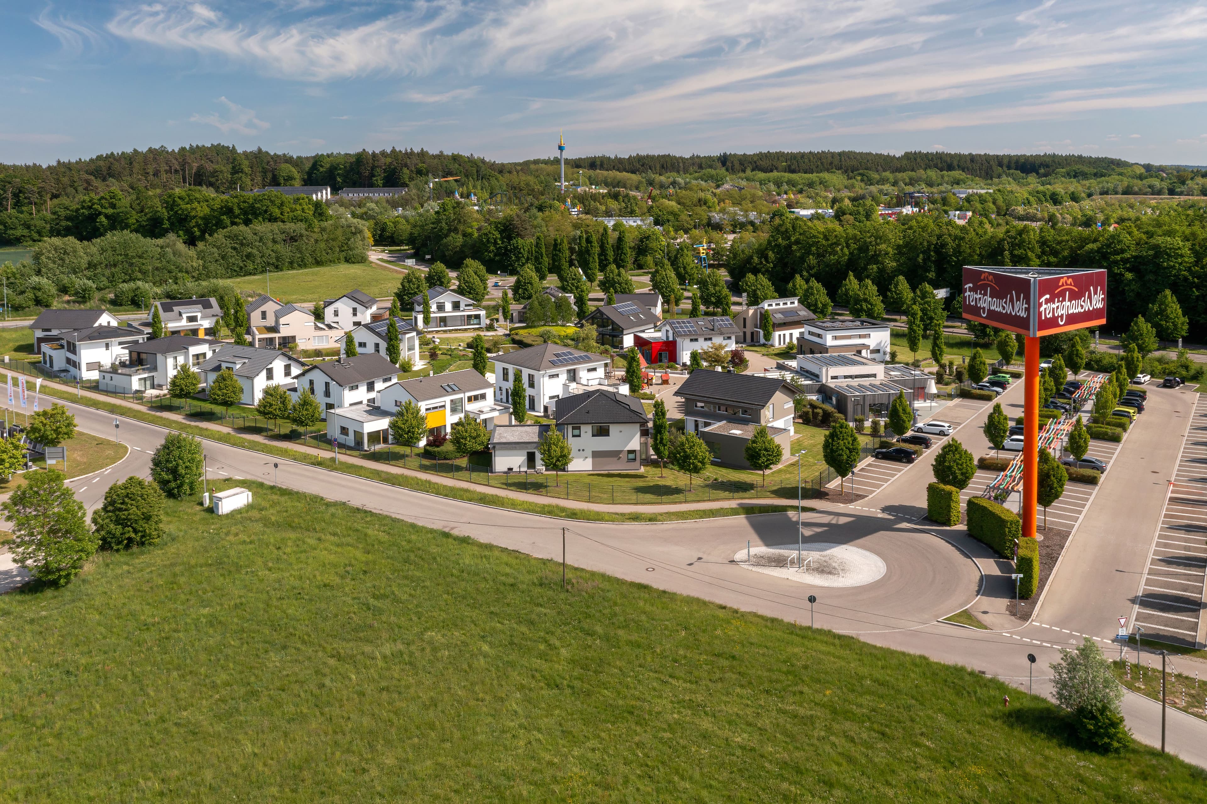 Luftaufnahme der FertighausWelt Günzburg mit modernen Musterhäusern, Straßen, Bäumen und Parkplatz.