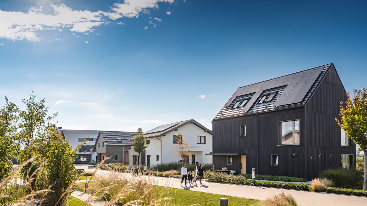 Moderne Wohnsiedlung mit schwarzem Einfamilienhaus, Solarpanelen und Familie auf gepflastertem Weg.
