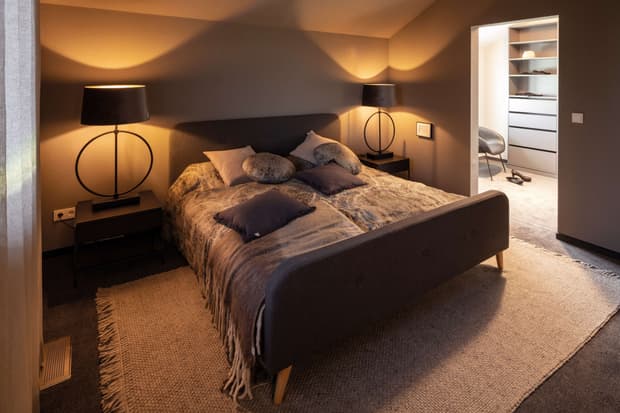 Gemütliches Schlafzimmer im modernen Musterhaus mit Doppelbett, warmem Licht, Teppichboden und begehbarem Kleiderschrank.