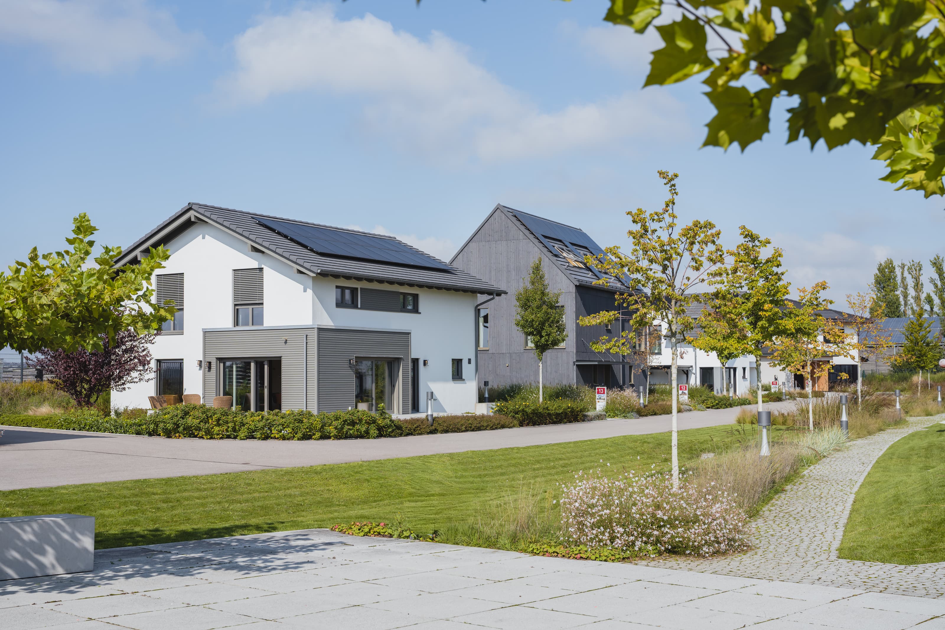 Modernes Einfamilienhaus mit Glasfassade, Balkon und überdachter Terrasse in sonnigem Garten.