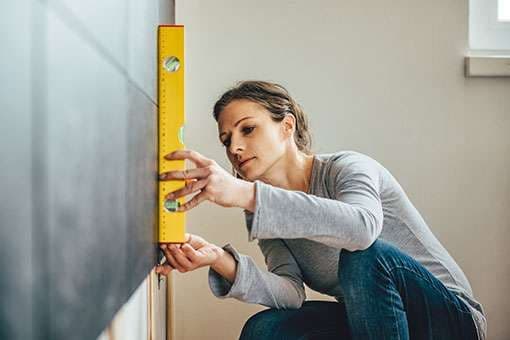 Frau begutachtet eine Wand mit einer Wasserwaage