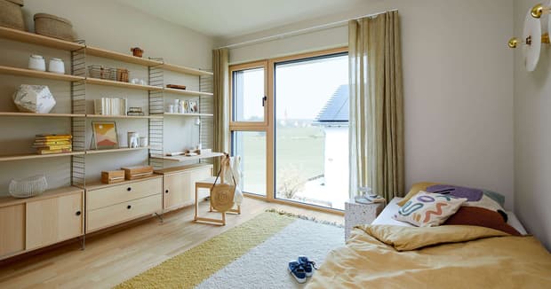 Helles Kinderzimmer im modernen Musterhaus mit Holzregalen, Bett, großem Fenster, Vorhängen und gemütlicher Einrichtung.