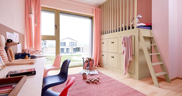 Helles Kinderzimmer im modernen Musterhaus mit Hochbett, Schreibtisch, rosa Wänden, Teppich und großem Fenster mit Ausblick.