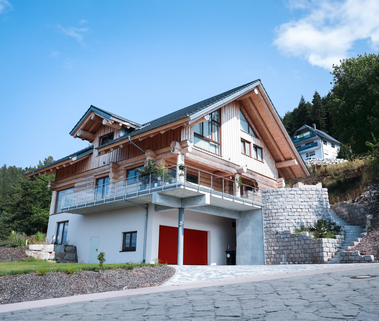 Modernes Alpenhaus mit roter Garage und Holzfassade in idyllischer Berglage. Luxuriöses Einfamilienhaus mit Balkon, Natursteinmauer und gepflegtem Außenbereich – perfekt für anspruchsvolles Wohnen in den Bergen.