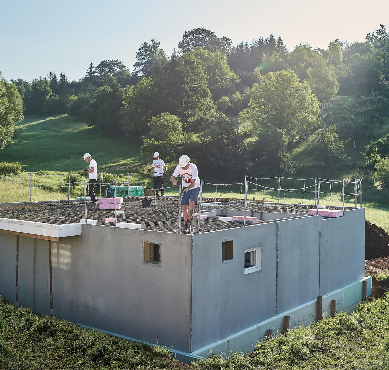 Hausbau in Massivbauweise: Bauarbeiter errichten Betonhaus mit Flachdach in grüner Landschaft. Professioneller Rohbau, moderne Bauweise und qualifizierte Handwerker für Ihr Traumhaus.
