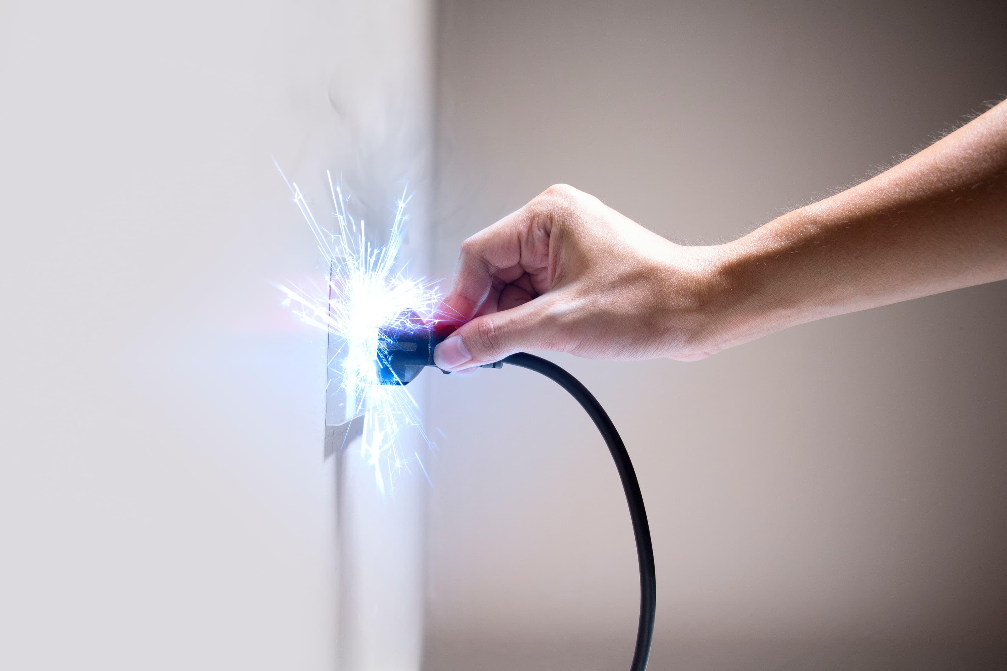 Hand steckt Stecker in Steckdose mit elektrischem Funkenflug – Symbolbild für Stromschlag, Elektrizität und Sicherheitsrisiken im Haushalt. Professionelles Foto zum Thema Elektroinstallation.