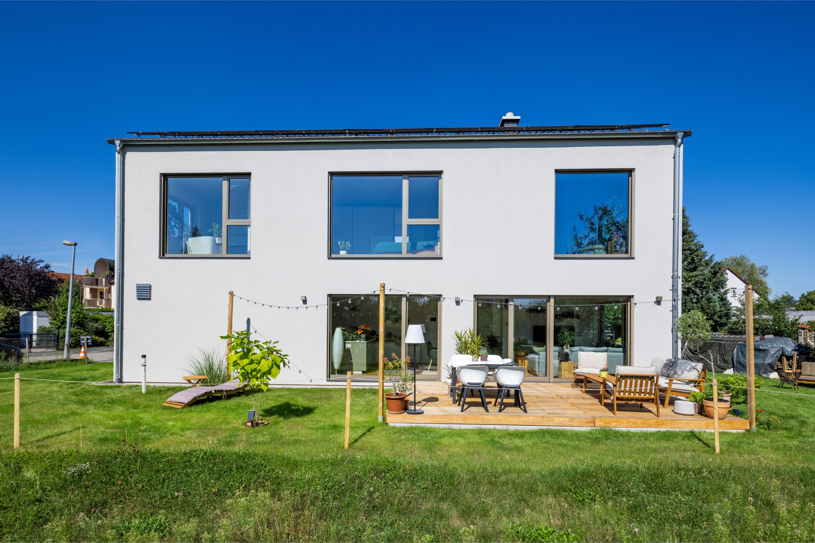 Modernes LUXHAUS Pultdachhaus in Weiß mit großer Holzterrasse, bodentiefen Fenstern und Garten bei blauem Himmel