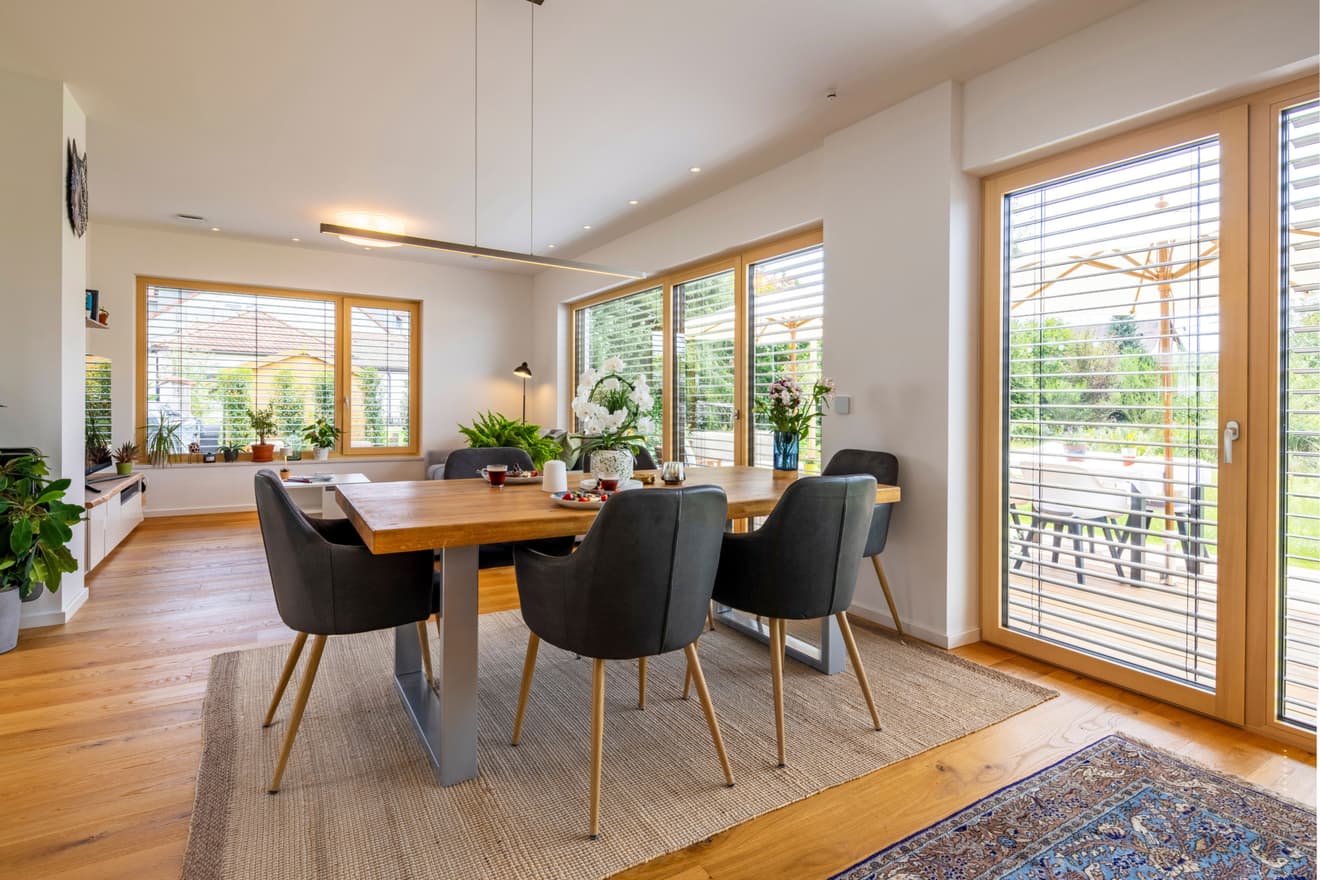 Lichtdurchfluteter Essbereich im LUXHAUS mit Holztisch, großen Fenstern mit Holzrahmen und Zugang zur Terrasse