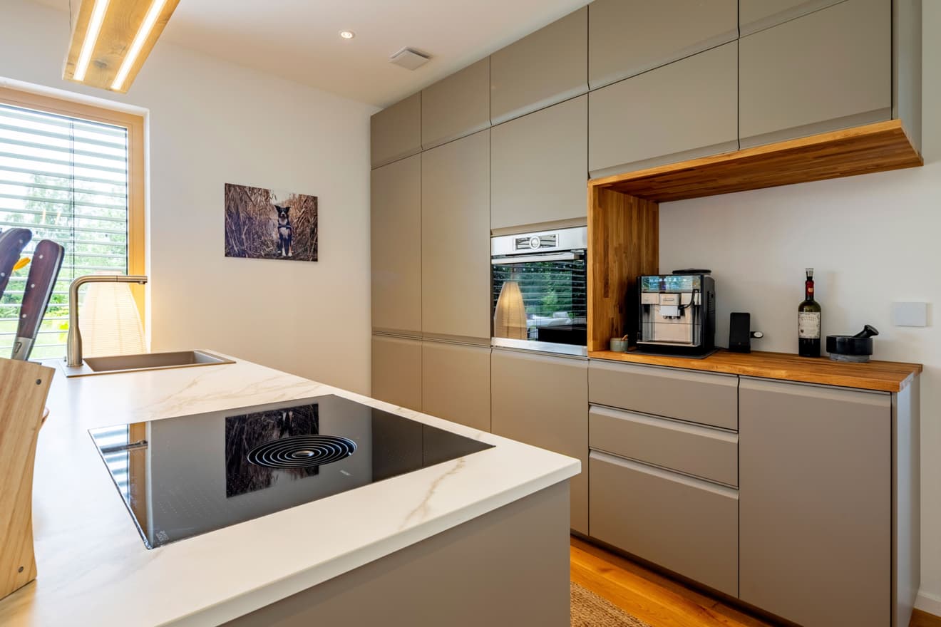 Moderne Küche im LUXHAUS mit Kochinsel, beigen Fronten, Holzakzenten und indirekter LED-Beleuchtung