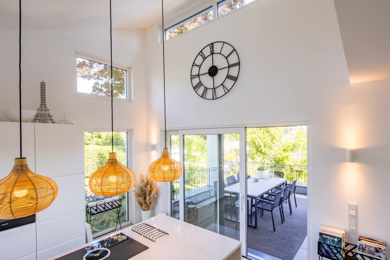 Moderne, helle Wohnküche mit hoher Decke, großer Wanduhr und warmen Pendelleuchten