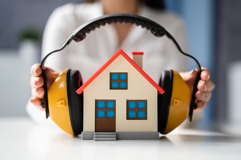 Miniaturhaus mit Kopfhörern als Symbolgrafik für den Schallschutz