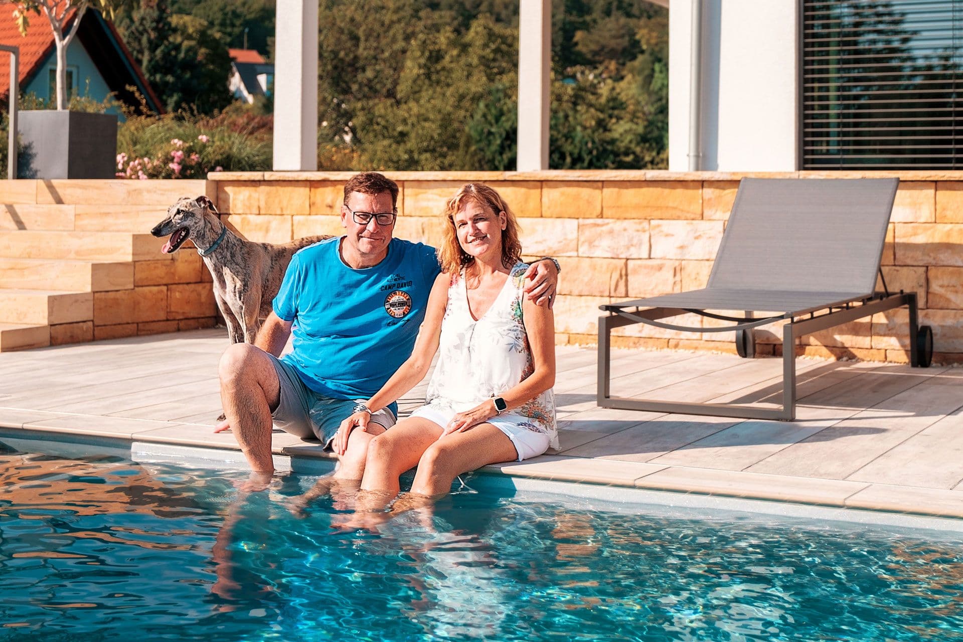 Baufamilie am Pool ihres Fertighauses mit Hund