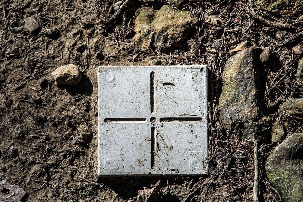 Grauer Messpunkt im Garten als Grundstücksbegrenzung