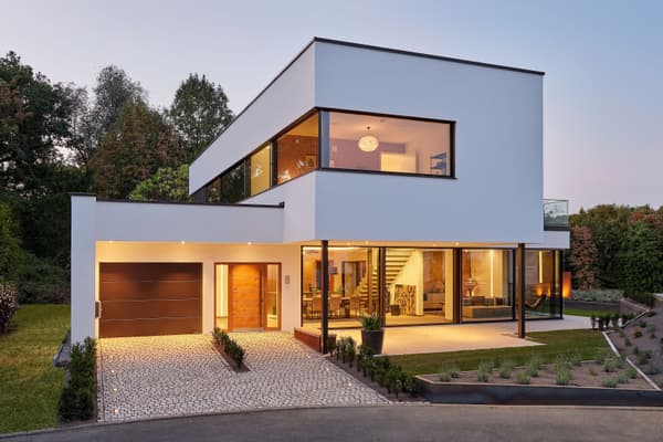 Modernes zweistöckiges Flachdachhaus mit großen Glasfronten, Garage, beleuchtetem Eingang und gepflegtem Vorgarten.