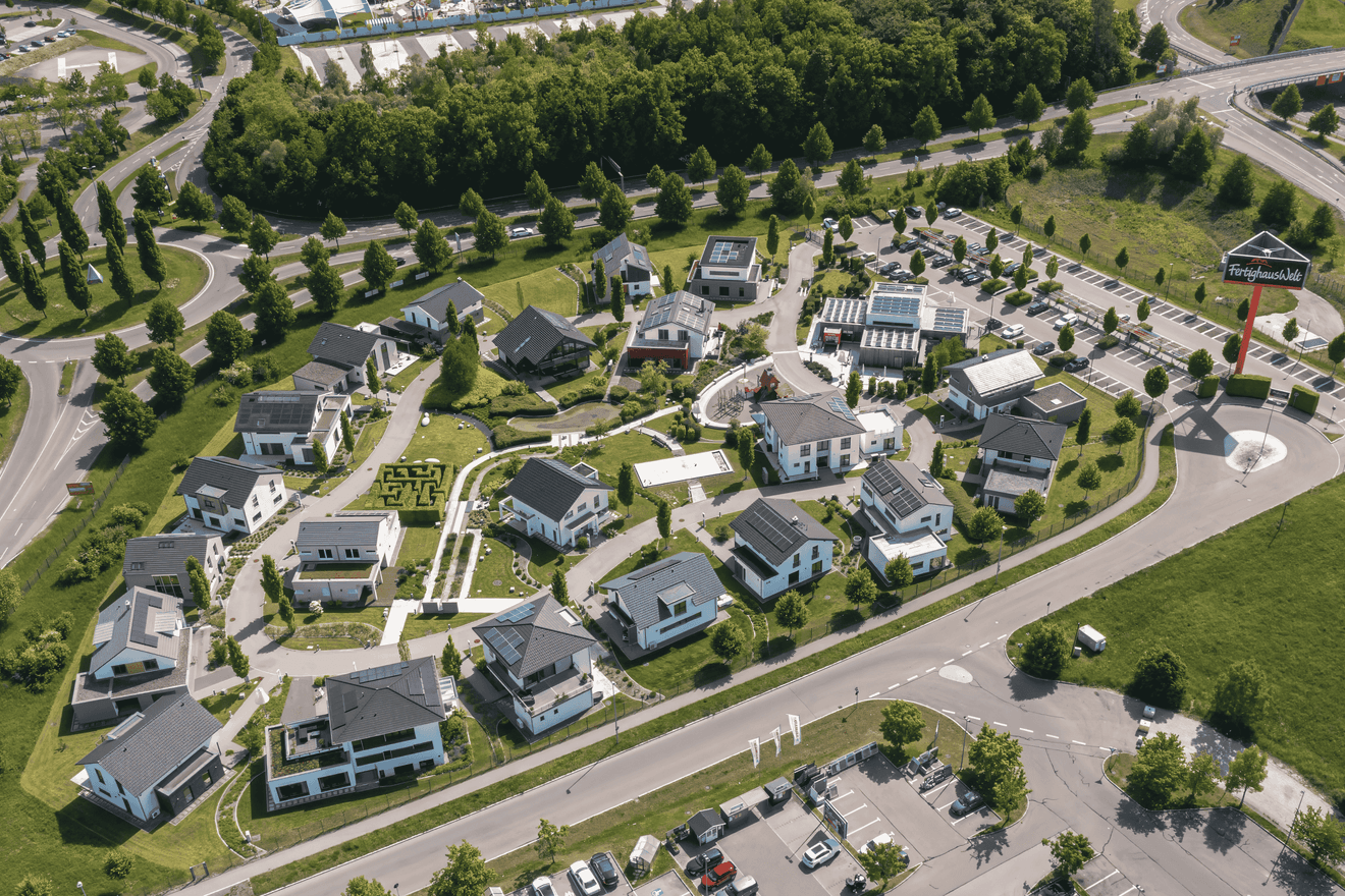 Luftaufnahme eines Musterhauses mit modernen weißen Einfamilienhäusern, Solarpanels und Grünflächen bei Sonnenschein